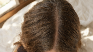 Close-up van boven van een scheiding in bruin haar met enkele zilveren haren in zacht ochtendlicht, Nutrafol voor vrouwen bij dunner haar in de overgang
